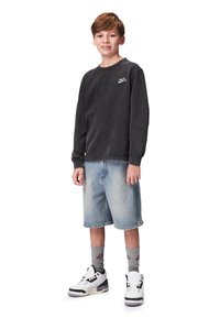 Harmaa pitkähihaine T-paita, farkkushortsit, harmaat sukat ja valkoiset sneakersit. Käsittää logon rinnassa, rento istuvuus ja vaaleansinisiä haalistuneita shortsit.