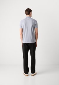 Camisa polo gris claro con mangas cortas, cuello clásico y una textura suave, combinada con pantalones negros y zapatillas blancas.