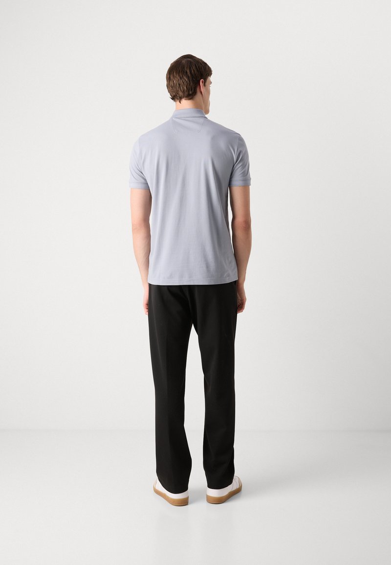 Hellgraues Poloshirt mit kurzen Ärmeln, klassischem Kragen und glatter Textur, kombiniert mit schwarzen Hosen und weißen Sneakers.