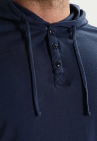 Granatowa bawełniana bluza z kapturem z regulowanym sznurkiem, zapinana na guziki, z fakturowanym przeszyciem w okolicach kołnierza.
