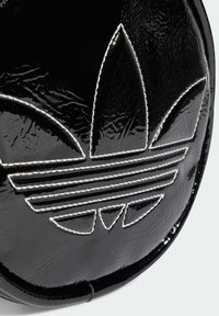 Borsa a tracolla circolare nera con finitura in patinato testurizzato, adornata da cuciture bianche e un evidente design del logo Adidas.