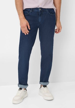 Dunkelblaue Denim-Jeans mit schlanker Passform, ausgestattet mit umgeschlagenem Saum und klassischem Fünf-Taschen-Design. Kombiniert mit weißen Sneakers.