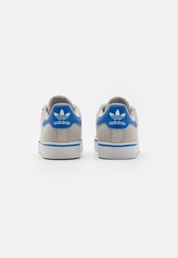 Grå sneakers med blå detaljer, övre del i slät tyg, vit sula och adidas-logotyp på hälen. Minimalistisk design, lågskuren stil.