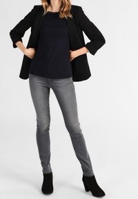 Svart kavaj över en marinblå topp, kombinerat med gråa tajta jeans och svarta ankelboots. Har en figurnära design och subtil textur.