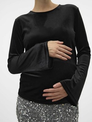 Must beega pikkade varrukatega must topp, mis on valmistatud pehmest materjalist, ümara kaelusega ja laienevate hõlmikutega, kombineeritud sädelevate hallide seelikuga. Käsi on asetatud kõhu peale.