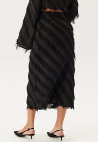 Svart midikjol med fransar och växlande satäng- och texturerade ränder, med en hög slits och en åtsittande midja. Stylerad med spetsiga flats.