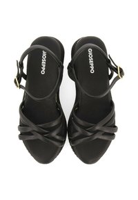 Sandalias negras con correa ajustable en el tobillo, suela plana y correas texturizadas entrecruzadas. Presenta detalles de hardware en tono dorado.