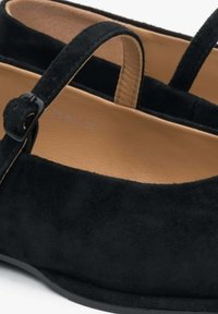 Czarne zamszowe buty o zaokrąglonym nosku, z paskiem na kostce i gładkim, jasnobrązowym wnętrzem. Posiadają płaską podeszwę oraz prosty, elegancki design.