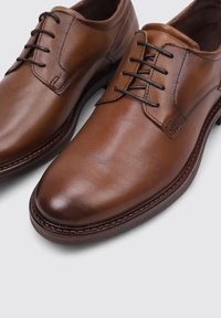 Zapatos de vestir de cuero marrón con un acabado suave, puntera redonda y diseño de cordones de cinco ojales. Presentan costuras en contraste y una suela resistente.