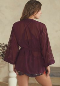 Kimono di un profondo viola con tessuto trasparente e dettagli in pizzo sulle maniche. Si lega in vita e presenta una parte inferiore floreale.