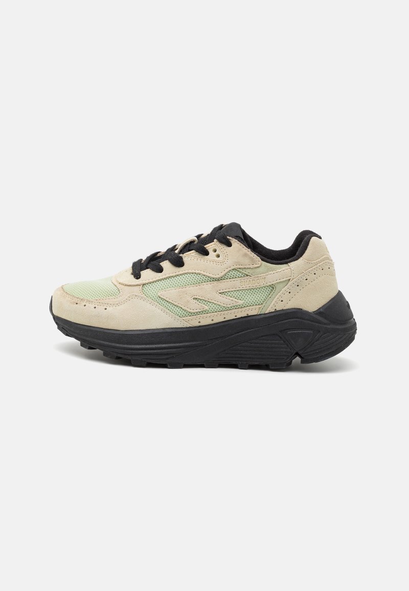 Baskets en suède beige et vert avec une semelle noire. Les caractéristiques incluent un design à lacets, des accents en mesh et une branding minimaliste sur le côté.