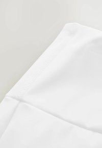 Tessuto bianco, texture liscia con una leggera lucentezza. La chiusura mostra i dettagli delle cuciture lungo il bordo, evidenziando linee pulite e un design minimale.