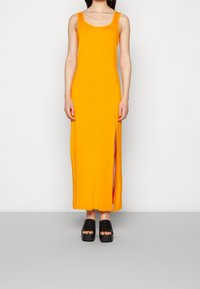 Maxi sukienka w jaskrawym pomarańczowym kolorze, z dekoltem w serek i bocznym rozcięciem. Połączona z masywnymi czarnymi sandałami na platformie.