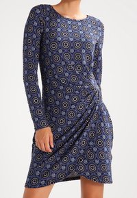 Long-sleeve dress made of soft, stretchy fabric featuring a blue and white circular pattern, with a gathered side detail for shaping.