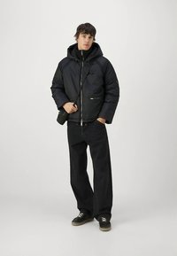 Czarna kurtka puchowa z kapturem, suwakiem i przednimi kieszeniami. Noszona z czarnymi spodniami o szerokich nogawkach i czarnymi butami. Casualowy, funkcjonalny design.