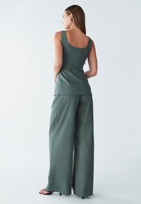 Groene top zonder mouwen met een vierkante achterkant, gecombineerd met losse, wijd uitlopende broek. Gladde textuur, minimalistisch ontwerp, effen stof.