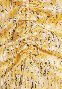 Gul tyg med en texturerad, samlad design som har växlande ränder och abstrakta mönster i svart och vitt.