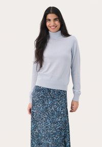 Light blue turtleneck sweater in soft fabric with long sleeves, paired with a patterned, flowing blue skirt featuring abstract designs.