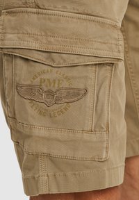 Bež kratke hlače od cargo tkanine s teksturiranim materijalom, više džepova i krilatim logotipom s natpisima "PME" i "Flying Legend" u bočnoj strani.