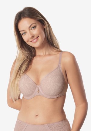 Młoda kobieta z długimi włosami, ubrana w dopasowany biustonosz i majtki w odcieniach nude z subtelnymi wzorami liści, uśmiechająca się na białym tle.