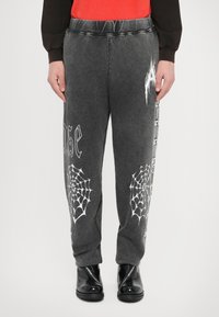 Szare spodnie dresowe o luźnym kroju, z grafikami białej pajęczyny i napisami na lewej nogawce, z elastycznym pasem i gładkim materiałem.
