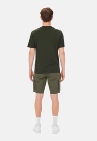 Camiseta de algodón verde oscuro y pantalones cortos de carga olivo con bolsillos laterales, combinados con zapatillas blancas y calcetines de longitud media.