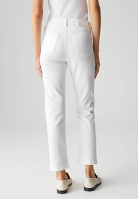 Witte straight-leg jeans met achterzakken en een schone tailleband. De stof lijkt zacht met een lichte glans. Draagt met lichtgekleurde schoenen.