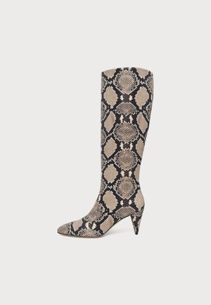 Botte haute beige et noire à motif peau de serpent, avec un bout pointu et un talon haut et fin, sur un fond uni.