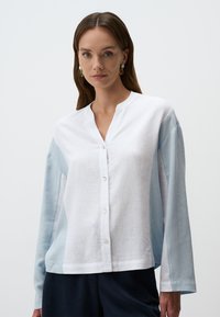 Camicia button-up in misto cotone bianco e azzurro chiaro, con maniche lunghe, scollo a V e una combinazione di texture. Lucentezza sottile sul tessuto.