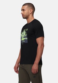 Zwarte katoen t-shirt met een voorkant graphic in het groen, met tekst en bergafbeeldingen. Korte mouwen en ronde hals.