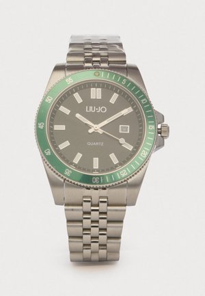 Ρολόι από ανοξείδωτο ατσάλι με πράσινη στεφάνη, γκρι καντράν και ασημένιες λεπτομέρειες. Διαθέτει κίνηση quartz και παράθυρο ημερομηνίας στις 3 η ώρα.