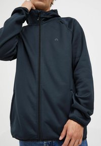 Laivin zip-up takki, jossa on huppu, valmistettu sileästä kankaasta. Ominaisuuksiin kuuluu tyylikäs muotoilu, sivutaskut ja pieni logo rinnassa.