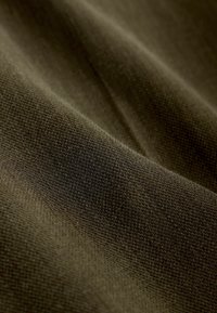 Tissu texturé en vert olive foncé, présentant un motif tissé avec des fils visibles et une finition douce et mate. Légère brillance par endroits.