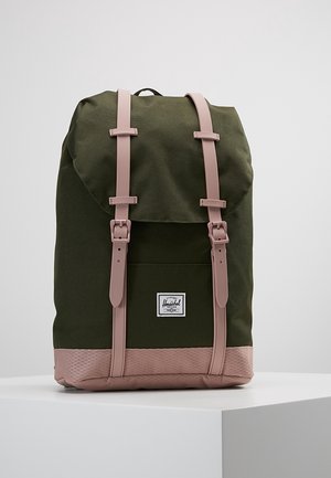 Zielony plecak z różowymi paskami i spodem, wyposażony w dwa zapięcia na klamry oraz białą metkę z przodu kieszeni, wyeksponowany na białej powierzchni.