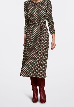 Woman wearing a patterned midi dress with 3/4 sleeves and a tie waist, paired with knee-high burgundy leather boots.