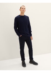 Marineblauer Strickpullover mit Rundhalsausschnitt, kombiniert mit dunklen Jeans und schwarzen Schnürstiefeln. Einfaches, strukturiertes Design mit lockerer Passform.