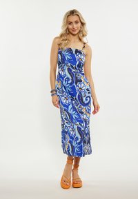 Rochie maxi albastră cu un model floral în diverse nuanțe, având bretele subțiri și un decolteu drept. Asortată cu sandale cu platformă portocalii cu curele.