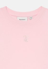 Rozā kokvilnas t-krekls ar apaļu kakla izgriezumu un īsām piedurknēm. Priekša rotāta ar rhinestone izšūtu logo. Etiķete vēsta "Juicy Couture."