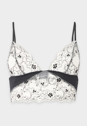 Biely čipkový bralette s čiernou kvetinovou výšivkou, tenkými čiernymi nastaviteľnými ramienkami a čiernou spodnou páskou s členitými okrajmi.