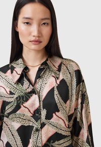 Blusa di seta con base nera, grande stampa botanica in verde e rosa, abbottonatura frontale e colletto con vestibilità rilassata.