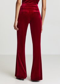 Pantalon évasé en velours rouge à taille haute, doté de poches latérales et d'une texture lisse et douce. Coupe longueur totale allant jusqu'au sol.