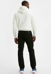 Svarta jeans med smal passform och bakfickor, i kombination med en vit hoodie. Hoodien har en dragsko och en framficka av kangurotyp.