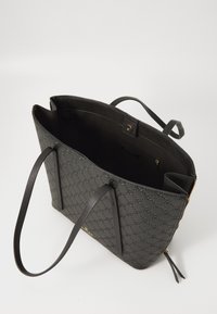 Sac fourre-tout noir avec motif embouti, texture lisse, doubles poignées et fermeture éclair. L'intérieur comporte une poche pour l'organisation.
