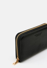 Schwarze Leder-Portemonnaie mit Reißverschluss rundherum, goldfarbenem Reißverschluss und geprägt eingraviertem Markennamen auf der Vorderseite, präsentiert vor weißem Hintergrund.