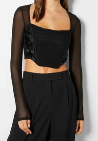Top nero aderente con texture arricciata e maniche lunghe trasparenti. Presenta un dettaglio in pizzo sui lati e uno scollo quadrato.