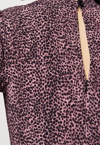 Růžová látka se vzorem černé leopardí kožešiny, se zadním výstřihem a malým černým knoflíkovým detailem na krku.