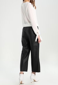 Blusa blanca y transparente con mangas largas y detalles de lazo; combinada con pantalones cortos de cuero negros y botines blancos de tacón alto.