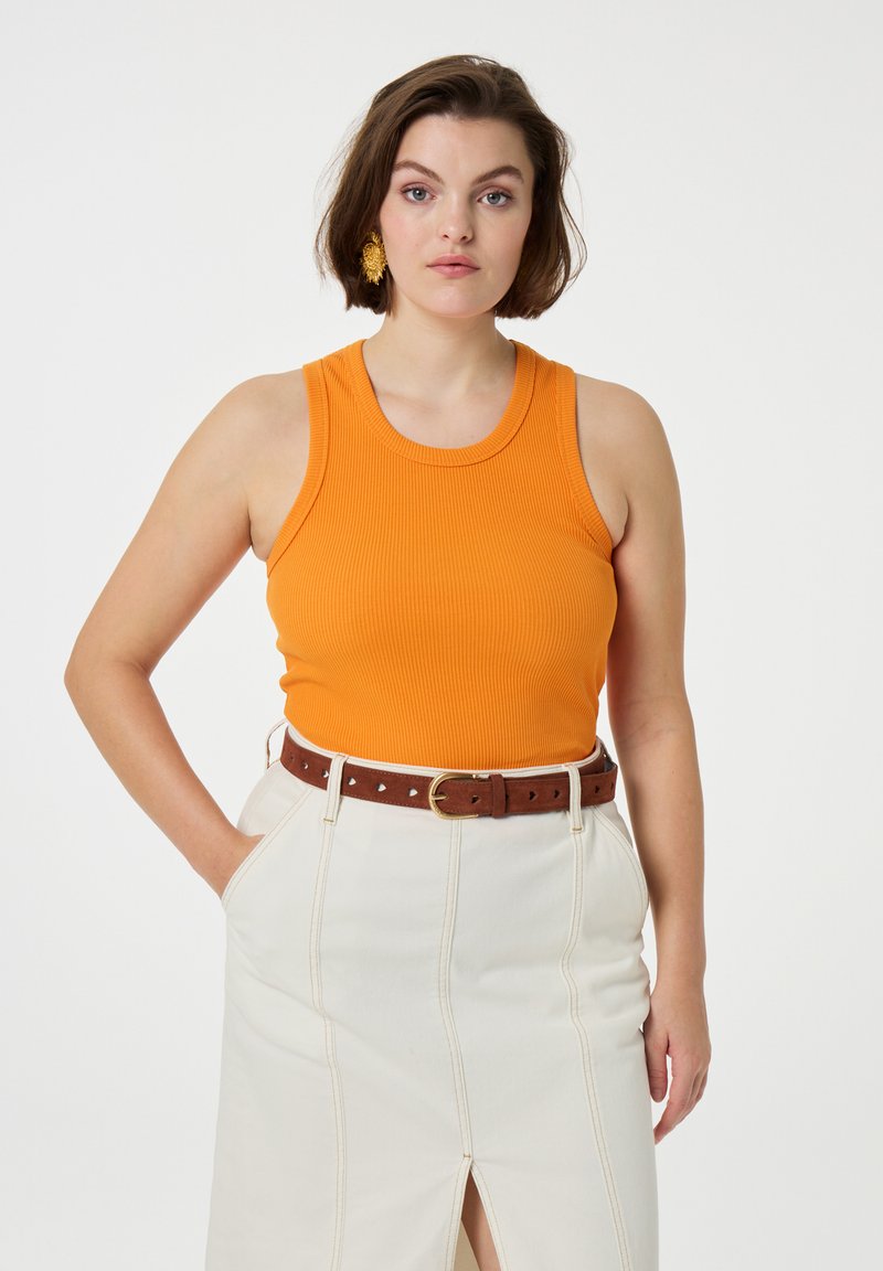 Ribbed orange tank top with a round neckline, paired with a white skirt featuring a front slit and a brown belt with heart-shaped cutouts.
