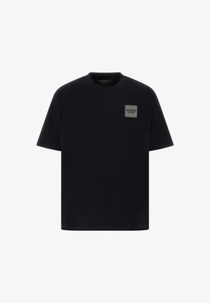 Czarna bawełniana koszulka z krótkim rękawem, z prostokątną szarością naszywką z logo po lewej stronie klatki piersiowej. Projekt z okrągłym dekoltem, gładka tekstura.