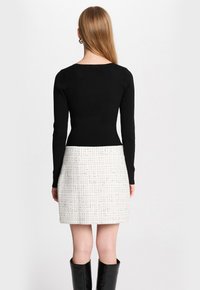 Haut noir à manches longues côtelé associé à une jupe blanche en tweed avec un motif à carreaux texturé. Des bottes noires montantes complètent l'ensemble.